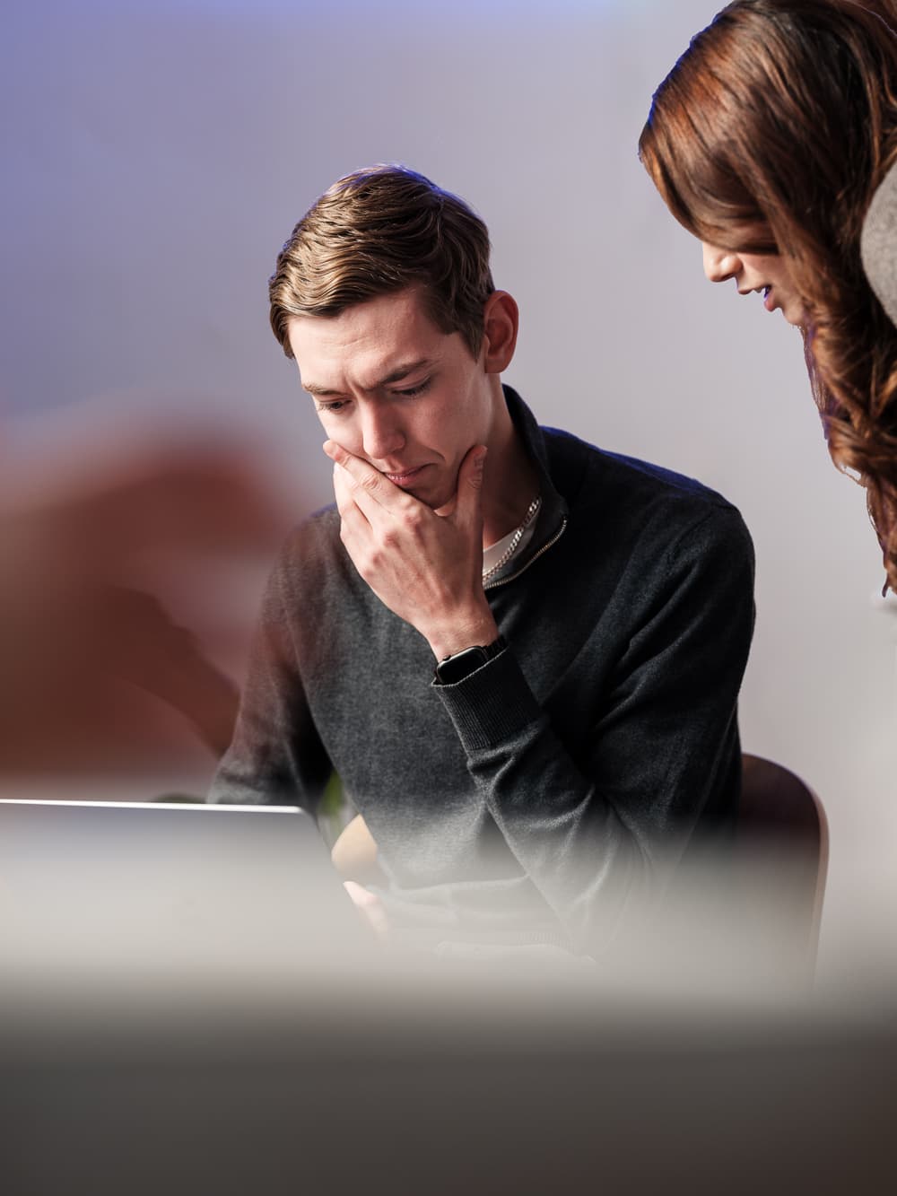 Person som sitter och ser fundersam ut framför en laptop och en tjej som står bredvid