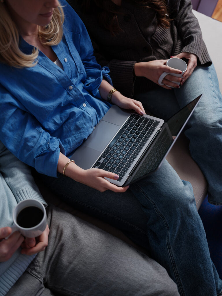 Tre personer som sitter i soffan, en person i mitten som håller i laptop och de två andra på sidan har en kaffekopp i handen.