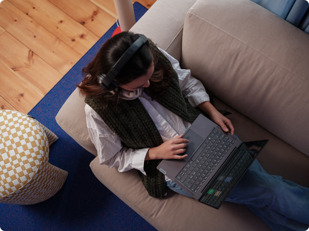Tjej som sitter med laptop och stora hörlurar på en soffa.
