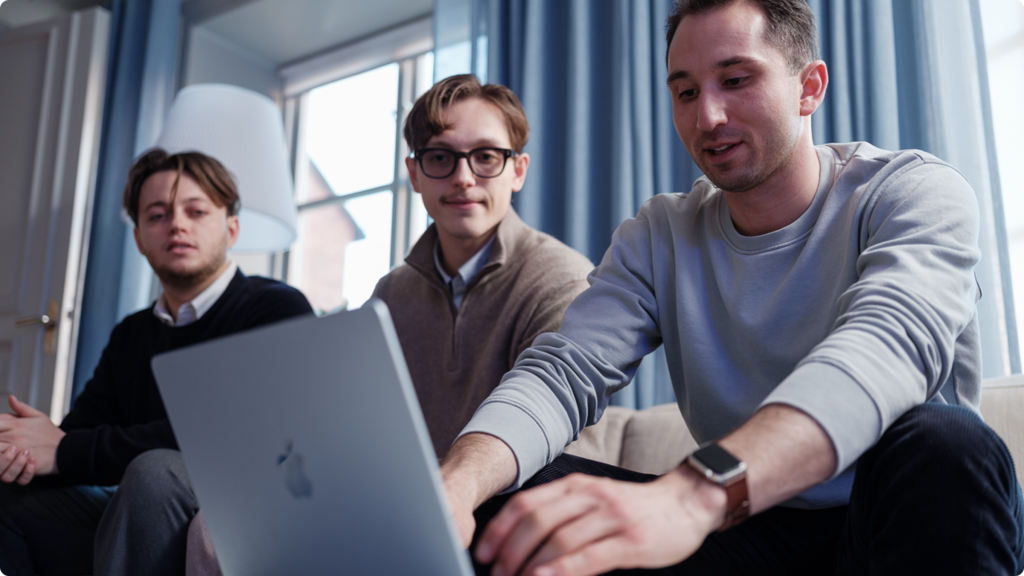 Tre personer som sitter vid en laptop. En person skriver på datorn.