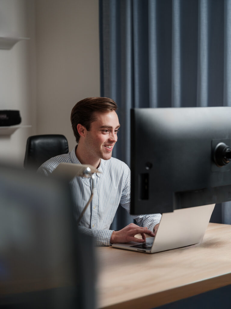 Kille som sitter framför laptop och dataskärm