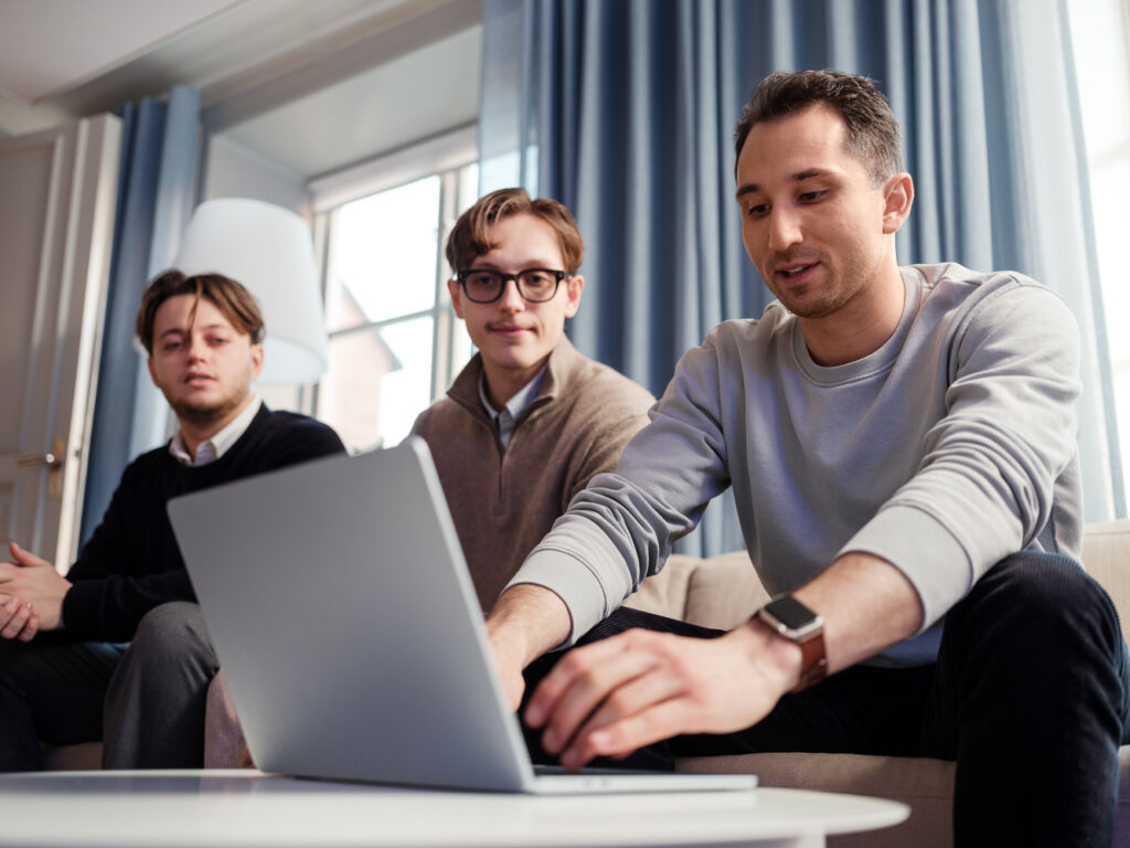 Tre personer som sitter vid en laptop. En person skriver på datorn.