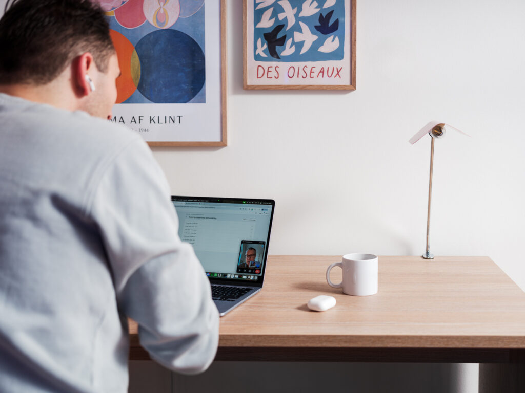 Kille som jobbar med laptop vid ett skrivbord och har möte via länk.